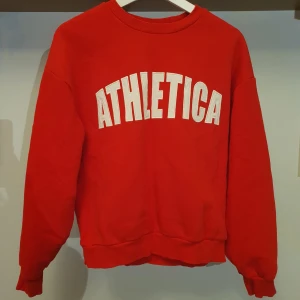 Röd sweatshirt från Gina Tricot - Säljer en snygg röd sweatshirt från Gina Tricot med texten 'ATHLETICA' i vitt på framsidan. Tröjan har en klassisk rund hals och långa ärmar, perfekt för en casual look. Den är i bra skick och superbekväm att ha på sig. Perfekt till vardags, på gymmet eller att mysa i hemma 💛 passar storlek XS och S 