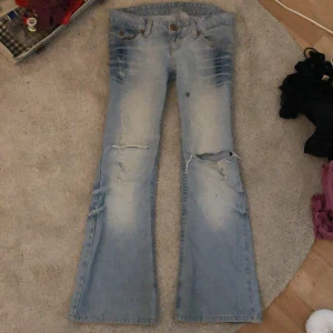 Ljusa jeans med slitningar -  Säljer ett par ljusa jeans med slitningar och hål på knäna. De har en klassisk femficksdesign och knappar i midjan. Perfekta för en avslappnad stil. Byxorna har en nagel lim fläck som man ser på tredje bilden vet inte om den går att få bort. Midjemått rakt över 41cm. Innerbenslängd 73cm