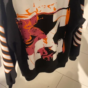 Svart  Off-White hoodie  - Snygg svart Off-White hoodie med ett stort grafiskt tryck i orange, rosa och vitt på ryggen.  Använd bara ett par gånger. Super bra skick.  Pris kan diskuteras !