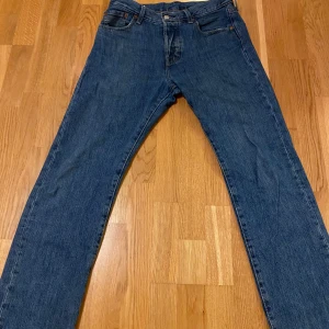 Levi's 501 jeans - Säljer ett par klassiska Levi's 501 jeans i blå denim. De har en straight passform och är i mycket bra skick. Perfekta för både vardag och fest! Midjan är midwaist och de har den ikoniska knäppningen framtill. Passar till alla säsonger och är ett måste i garderoben.