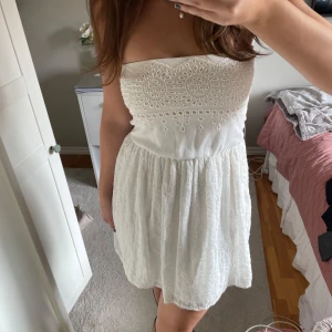 Vit axelbandslös klänning från Zara - Säljer en söt vit axelbandslös klänning från Zara med broderade detaljer på överdelen. Perfekt till student!  