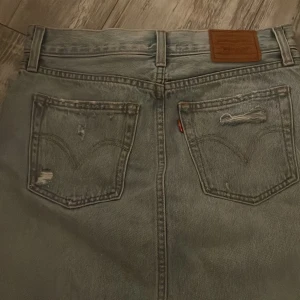 Jeanskjol från Levi's - Jeanskjol från Levi's med slitna detaljer. Den är aldrig använd så den är i nyskick, och tror inte modellen finns kvar längre❤️skriv om ni har frågor!