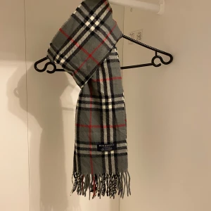 Burberry - Säljer nu denna Snygga halsduk från Burberry i färgen grå. Tillverkad i 100% mjuk kashmir med klassiskt fransad kant. Perfekt för att hålla dig varm och stilren under kyliga dagar. Hör av er vid funderingar☺️