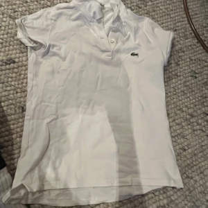 Vit kortärmad pikétröja från Lacoste - Säljer en klassisk vit pikétröja från Lacoste med korta ärmar och knappdetalj vid halsen. 