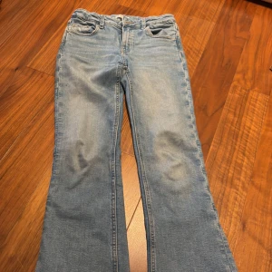 Blå jeans från Gina Tricot - Säljer ett par snygga blå jeans från Gina Tricot i storlek 152. De har en klassisk femficksdesign och en knappgylf. Perfekta för en avslappnad stil, med låg midja.