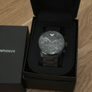 Svart klocka från Emporio Armani - Hej! Säljer min Armani klocka. Har haft den i 6 månader nu och det är dags att bli av med den. Som ni ser i bilden har den inga rep märken. Du kan justera den också om den inte passar dig som ni ser i bild 3 så finns det också en extra batteri för klockan som håller              i 1,5-2 år. Tveka inte på att skriva om ni är intresserade.