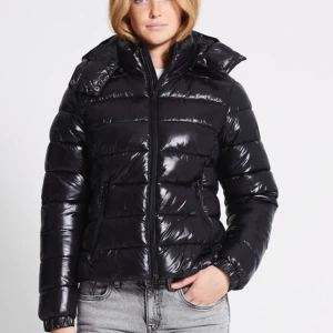 Svart pufferjacka med huva Nikki lager 157 storlek S - Snygg svart pufferjacka med glansig finish och praktisk huva. Jackan har dragkedja framtill och långa ärmar, perfekt för kyliga dagar. En stilren och varm jacka för vintersäsongen.