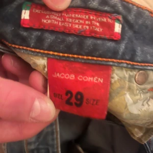 Blå jeans från Jacob Cohen - Snygga blå jeans från Jacob Cohen med klassisk femficksdesign och en unik läderpatch baktill. Jeansen har en normal passform och är tillverkade i Italien, vilket ger dem en exklusiv känsla.