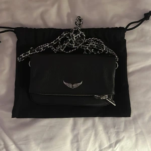 Svart axelväska från Zadig & Voltaire - Snygg svart axelväska i skinn från Zadig & Voltaire med silverfärgad kedja och dragkedja. Liten och bra får plats med mer än man tror. Använd få gånger, då den inte passar mina guld smycken. 