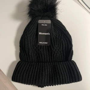 Stickad mössa - Snygg svart stickad mössa med en fluffig pälsboll på toppen. 