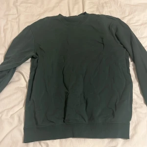 Grön sweatshirt från H&M - Säljer en grön crewneck sweatshirt från H&M i relaxed fit. Perfekt för en avslappnad stil med ribbade muddar vid ärmslut och nederkant. Enkelt och stilrent plagg för vardagsbruk.