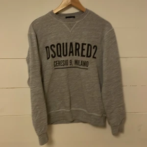 Grå sweatshirt från DSQUARED2 - Säljer en stilren grå sweatshirt från DSQUARED2 med tryck på framsidan. Tröjan har långa ärmar och ribbade muddar vid ärmslut och nederkant. Perfekt för en avslappnad look. 9/10 skick inga defekter. Ny pris 1200kr. Mitt pris 499kr