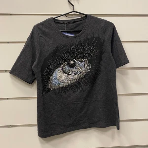 Vintage T-Shirt boxy - T-Shirt med boxy passform ifrån Wico. Ögat är täckt med massa paljetter i olika färger. Storlek Medium med en melerad mörkgrå färg.