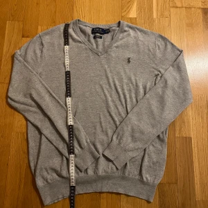 Ralph Lauren tröja grå - Säljer en stilren grå tröja från Ralph Lauren med v-ringning och broderad logga på bröstet. Tröjan är i bomull och är varm,skön och snygg. Perfekt som ett skönt och stilrent lager under jackan nu när vintern är på väg. Skick 9/10. Mvh Carl