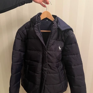 Mörkblå vinterjacka  - Snygg Mörkblå Vinterjacka med huva och dragkedja. Köptes på rea för 599kr, originalpriset låg på 1199kr per jacka. Ralph Lauren märke på bröstet (ej äkta). Finns att köpa i storlek M. Kontakta om det är något du undrar eller om det önskas fler bilder:)   