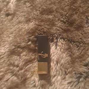 Läppstift från YSL - Elegant läppstift från YSL i nyansen 'The Bold 44'. Hylsan är svart med en lyxig guldig detalj och bas. Perfekt för att ge en djärv och sofistikerad look.