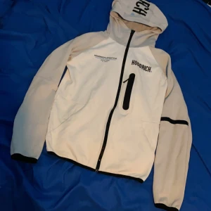 Vit/grå Hoodrich zip hoodie - Säljer en snygg vit/grå Hoodrich zip hoodie med svart text och detaljer. Storlek XS
