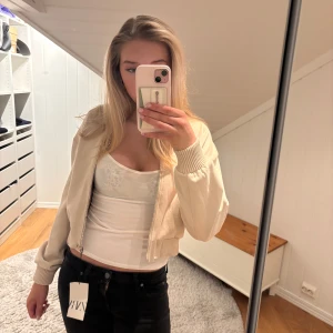 Beige bomberjacka - Säljer en snygg beige bomberjacka med dragkedja framtill. Jackan har långa ärmar och ribbade muddar vid ärmslut och nederkant. Perfekt för en stilren look.