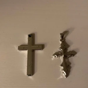 Två korsformade hängen i metall - Säljer två korsformade hängen i metall. Det ena är ett enkelt kors med en slät yta och det andra har en mer detaljerad design med spetsiga kanter. Perfekta för att skapa ett personligt halsband. 35 kr för båda.
