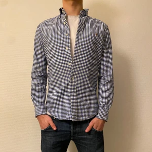 Blårutig skjorta från Polo Ralph Lauren - Snygg blårutig skjorta från Polo Ralph Lauren i slim fit. Skjortan har långa ärmar och knappar framtill. Den är broderad med det klassiska Polo Ralph Lauren-emblemet på bröstet.