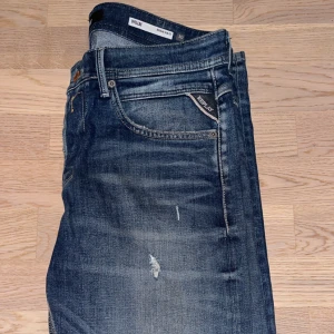 Blå jeans från Replay - Snygga blå jeans från Replay med en sliten look och diskreta slitningar. Klassisk femficksdesign och knappgylf. Perfekta för en avslappnad stil. Storlek 30-34 är i topp skick, endast använda 2 gånger. Nypris 1899.