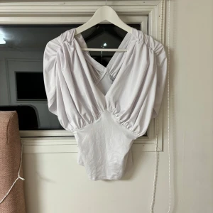 Vit topp från NA-KD - Säljer en stilren vit topp från NA-KD med djup v-ringning och draperade detaljer. Toppen har korta ärmar och en elegant design som passar perfekt för en trendig look.