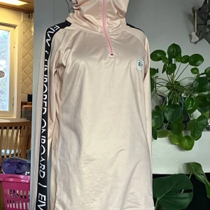 Ljusrosa tröja från Eivy - Säljer en ljusrosa tröja från Eivy med hög krage och dragkedja. Tröjan har långa ärmar med svarta detaljer och text längs ärmarna. Perfekt för kyligare dagar. Ursprungspris 799kr