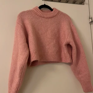 Rosa stickad croppad tröja - Säljer en söt rosa stickad tröja med croppad passform. Tröjan har långa ärmar och en ribbad kant vid halsen och nederkanten. Perfekt för en mysig och stilren look.
