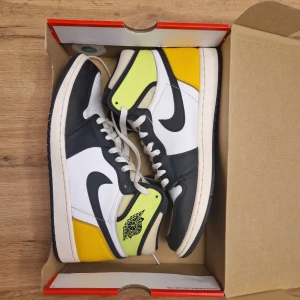 Nike Air Jordans i svart, vit och gul - Snygga Nike Air Jordans med en fräsch färgkombination av svart, vit och gul. Skorna har klassisk snörning och en hög siluett som ger ett sportigt intryck. Perfekta för dig som vill ha en stilren och iögonfallande look.