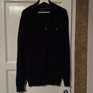 Svart half zip Gant - Snygg svart tröja från Gant med halv dragkedja och broderad logga på bröstet. Perfekt för en stilren look. Långärmad och bekväm passform.