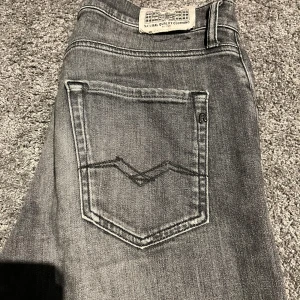 Grå jeansbyxor från Replay - Snygga grå jeansbyxor från Replay med klassisk femficksdesign och subtila slitningar. Byxorna har en rak passform och är perfekta för en avslappnad stil. Märkeslogga på bakfickan ger en extra touch. Jeansen passar dig som är emellan 170 och 180 cm lång. Modellen heter Thad. Tveka inte och höra av er för funderingar eller mer bilder.🙌🏻