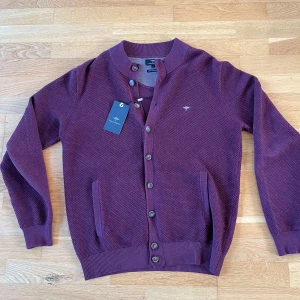 Vinröd kofta från fynch hatton  - Säljer en stilren vinröd kofta från fynch haton med knappar framtill. Koftan har långa ärmar och ribbade muddar. Nypris: 899 kr