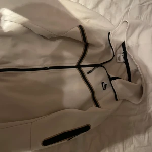 Vit hoodie från Nike, Size m , tjock  - Säljer en stilren vit hoodie från Nike med dragkedja och svarta detaljer. Perfekt för en sportig look eller avslappnade dagar. Den har en klassisk passform och är tillverkad i mjukt material för extra komfort.