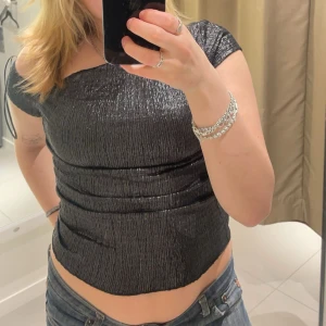 Svart glittrig topp - Snygg svart glittrig topp med korta ärmar och en tight passform. Perfekt för en kväll ute eller festliga tillfällen. Toppen har en elegant glans som fångar ljuset fint.