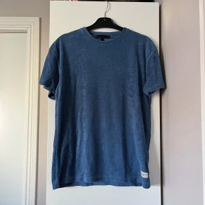 Blå frotté t-shirt från Mennace - Blå frotté t-shirt från Mennace. Märket sitter längst ner på tröjan. 