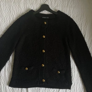Svart kofta från Atmosphere - Säljer en elegant svart kofta från Atmosphere med guldknappar och två små fickor framtill. Koftan har en rund halsringning och är perfekt för att ge en stilren touch till din outfit. Passar bra till både jeans och kjol. 🖤