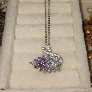 Svanformad halsband med glittriga stenar - Elegant halsband med en svanformad hängsmycke dekorerad med glittriga stenar i silver, lila och blå nyanser. Perfekt för att ge en touch av glamour till din outfit.