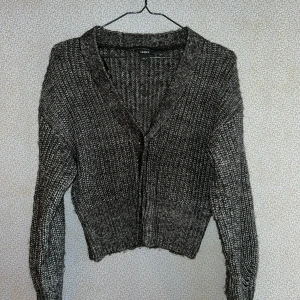 Grå stickad kofta från Lindex - Säljer en mysig grå stickad kofta från Lindex. Koftan har en v-ringad design och långa ärmar, perfekt för kyliga dagar. Den är ribbad och har en stilren look som passar till många olika outfits. Perfekt för höst och vinter!