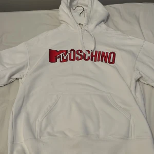 Vit hoodie från Moschino - Säljer en vit hoodie från H&M x Moschino med rött tryck på framsidan. Den har en klassisk känguruficka och justerbar huva med snören. Perfekt för en avslappnad stil. Passar S perfekt. Säljer då den är för stor på mig.