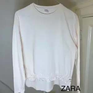Säljer en stilren vit långärmad tröja från Zara. Tröjan har en elastisk detalj vid nederkanten som ger en snygg passform. Perfekt för en avslappnad look.