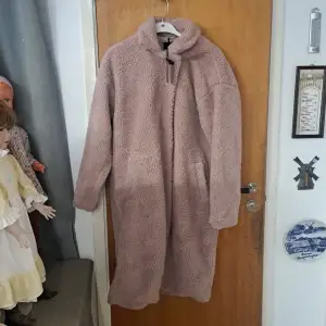 Mysig rosa teddyjacka från Lager 157 i storlek XS/S. Jackan har en lång och bekväm passform med hög krage och dragkedja framtill. Perfekt för kyliga dagar när du vill hålla dig varm och stilren.