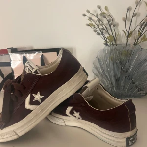 Vinröda Converse Star Player 76 - Trendiga vinröda Converse Star Player sneakers med klassisk design och vit sula. Skorna har snörning och den ikoniska stjärnloggan. Mycket bra skick. Slutsåld i denna färg och storlek. 