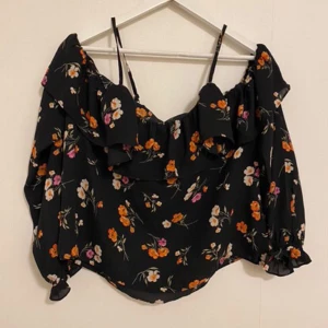 Blommig offshoulder topp från Gina Tricot - Säljer en söt blommig offshoulder topp från Gina Tricot.  Den har volangdetaljer och smala axelband med långa ärmar. Ser sliten ut på taggen annars inga defekter!