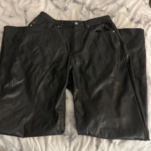 Svarta skinnbyxor - Snygga svarta skinnbyxor med en klassisk design. Byxorna har en rak passform och är perfekta för en stilren look. De har fickor både fram och bak samt knappar och dragkedja i gylfen.