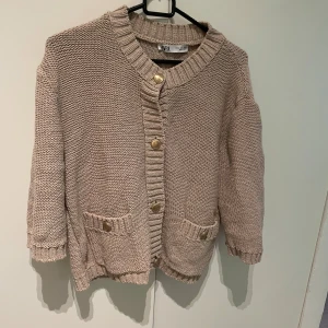 Beige stickad kofta från Zara - Mysig beige stickad kofta från Zara med guldknappar och två fickor framtill. Storlek XL men passar mer S-M för väldigt liten i storleken