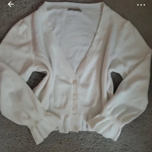 Vit kofta med knappar - Säljer en stilren vit kofta med knappar framtill. Den har långa ärmar och en v-ringad design, perfekt för lager på lager-stil. Passar bra till både jeans och kjol.