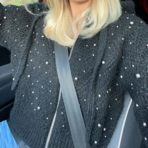 Svart stickad kofta med pärlor - Säljer en snygg svart stickad kofta dekorerad med pärlor. Koftan har en dragkedja framtill och långa ärmar. Perfekt för att ge en elegant touch till din outfit. Passar bra till både jeans och kjol. Finns även luva på den går ner till ca över höfterna och passar xs,s,m super