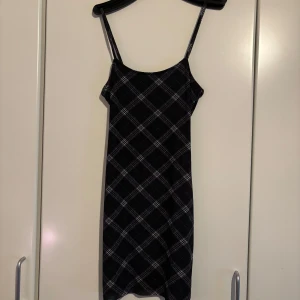 Svart och vit rutig klänning - Snygg svart/blå klänning med vita rutor och smala axelband. Perfekt för en stilren look. Klänningen har en enkel och elegant design som passar till många tillfällen.