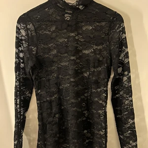 Svart spetsblus från Neo Noir - Elegant svart spetsblus från Neo Noir med långärmad design. Perfekt för en stilfull look med sitt spetsmönster. Blusen har en liten krage och är tillverkad i ett mjukt och bekvämt material.