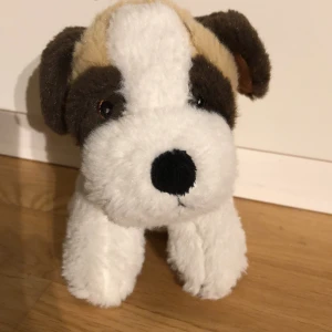 Mjukisdjur hund från Keenway - Söt och mjuk hund i plysch från Keenway. Den har en vit kropp med bruna och beige fläckar samt svarta detaljer. Perfekt för kramar och lek!